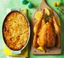 Roast chicken on a wooden board beside a dish of dauphinoise potatoes